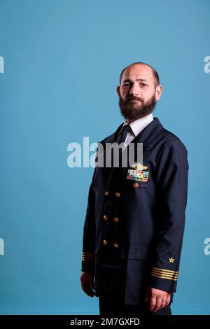 Flugzeugkapitän steht in professionellem, einheitlichem Porträt, selbstbewusster Flugzeugpilot steht, schaut in die Kamera, Studio mittlere Aufnahme, Seitenansicht. Zivilflieger mit Abzeichen auf der Jacke Stockfoto