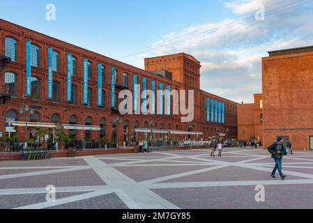 Lodz, Polen - 29. September 2022: Besucher besuchen den inneren Platz von Manufaktura bei Sonnenuntergang, ein Kunstzentrum, ein Einkaufszentrum und einen Freizeitkomplex Stockfoto