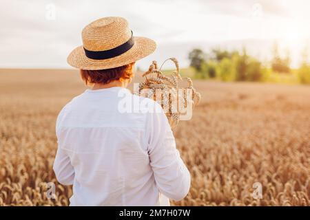 Rückansicht einer Farmerin, die bei Sonnenuntergang im Sommerfeld Weizen kontrolliert. Ernte in der Ukraine. Landwirtschaft und Landwirtschaft Stockfoto