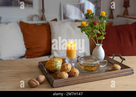 Tablett mit einer Tasse Tee, beleuchteten Kerzen und Herbstdekoration auf einem Tisch im Wohnzimmer, gemütliches Zuhause in der kalten Jahreszeit, Kopierraum, ausgewählter Fokus, text Stockfoto