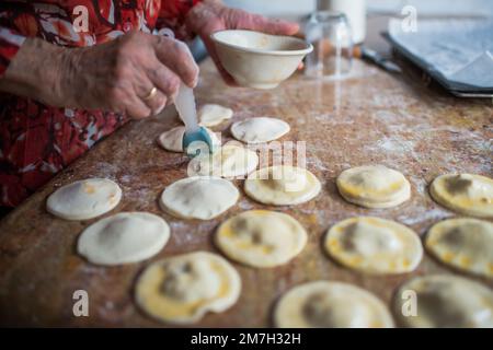 Nicht wiedererkennbare Alte Frau, die spanische Knödel mit Volleierfleisch überzieht. Innenraum Stockfoto