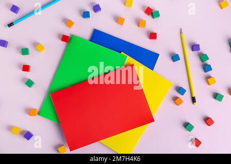 Komposition mit bunten Notizbüchern, Bleistiften und Würfeln auf pinkfarbenem Hintergrund Stockfoto