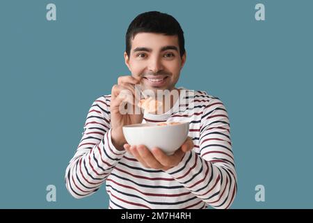Junger Mann isst Cornflakes mit Löffel auf farbigem Hintergrund, Nahaufnahme Stockfoto