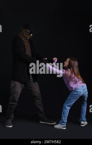 Terrorist und ängstliche kleine Geisel auf dunklem Hintergrund Stockfoto