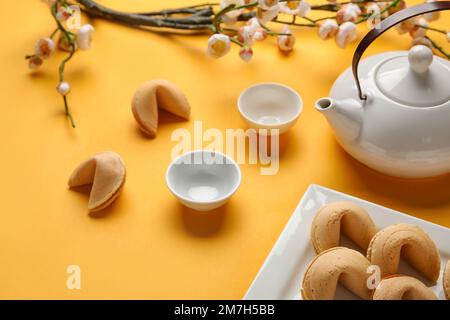 Glückskekse, Teekanne, Tassen und Sakura auf gelbem Hintergrund. Chinesische Neujahrsfeier Stockfoto