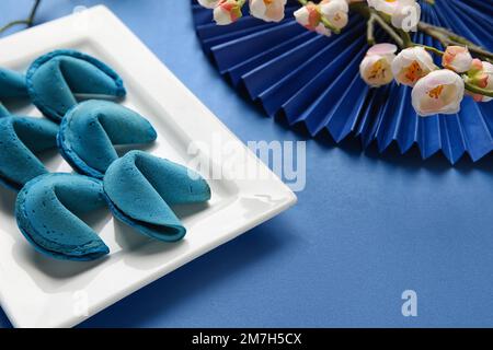 Teller mit Glückskeksen und chinesischen Symbolen auf blauem Hintergrund, Nahaufnahme. Neujahrsfeier Stockfoto