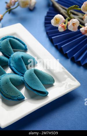 Teller mit Glückskeksen und chinesischen Symbolen auf blauem Hintergrund, Nahaufnahme. Neujahrsfeier Stockfoto