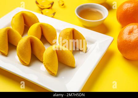 Teller mit Glückskeksen und Mandarinen auf gelbem Hintergrund, Nahaufnahme. Chinesische Neujahrsfeier Stockfoto