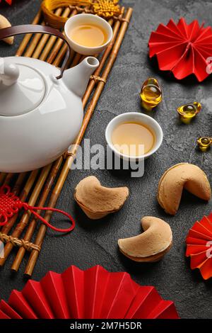 Glückskekse mit Teekanne, Tassen und chinesischen Symbolen auf dunklem Hintergrund. Neujahrsfeier Stockfoto