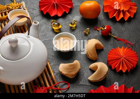 Glückskekse mit Teekanne, Tassen und chinesischen Symbolen auf dunklem Hintergrund. Neujahrsfeier Stockfoto
