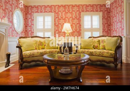 Runder hölzerner Couchtisch und gelb geblümte gepolsterte Sofas im Wohnzimmer im eleganten Haus im Cottage-Stil. Stockfoto