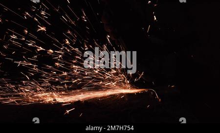 Helle Funken aus einer kreisförmigen Nahaufnahme im Dunkeln auf schwarzem Hintergrund. Ein Arbeiter schneidet Metall mit einer Nahaufnahme einer Kreissäge. Mit Eisen arbeiten. Stockfoto