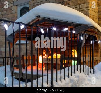 Beleuchtete Krippenbühne in St. Josephs katholische Kirche, die an einem verschneiten Winterabend durch ein Geländer mit einer Reihe von Weihnachtslichtern gesehen wird. Stockfoto