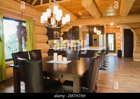 Esstisch aus braun gebeiztem Kiefernholz und Stühle aus braunem Leder mit hoher Rückenlehne im Speisesaal plus weiße Quarzplatte mit Lederbarhockern. Stockfoto