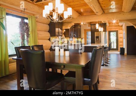 Esstisch aus braun gebeiztem Kiefernholz und Stühle aus braunem Leder mit hoher Rückenlehne im Speisesaal plus weiße Quarzplatte mit Lederbarhockern. Stockfoto