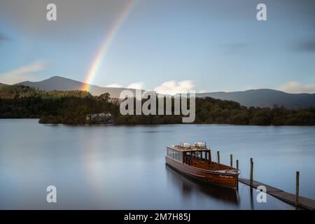 Lange Belichtung des Motorstarts Prinzessin Margaret Rose, die an der Keswick Landing Stage festsaß, mit einem Regenbogen über Derwent Isle im Hintergrund Stockfoto