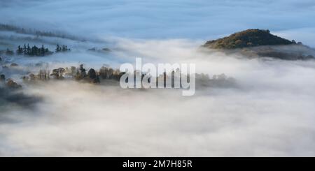 Castlerigg Manor und nahegelegene Häuser in Keswick erschienen aus einer Wolkeninvertierung kurz nach Sonnenaufgang mit Hügeln und Bäumen Stockfoto