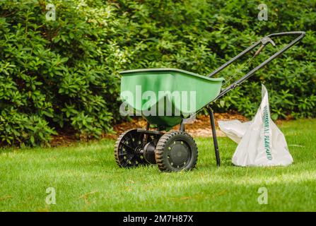 Handgeführt hinter einem Grassamenstreuer und einer Tüte mit Rasendünger in einem grünen Hinterhof. Stockfoto