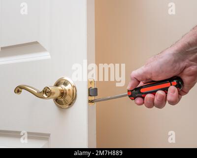 Zimmermann repariert Türschloss. Handwerker mit Schraubendreher zur Montage der Befestigungsteile der Türverriegelung. Stockfoto