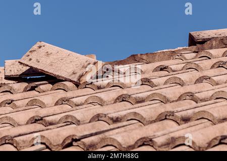 Hurricane beschädigte zerbrochene Spanische Dachziegel mit blauem Himmelshintergrund. Ziegeldach für Wohngebäude, das repariert oder ersetzt werden muss. Stockfoto