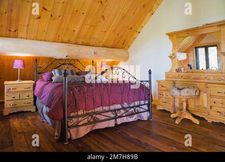 Queen-Size-Bett mit schmiedeeisernem Kopfteil und Fußbrett plus antike Holzschränke im Hauptschlafzimmer im oberen Stockwerk in einer luxuriösen Blockhütte. Stockfoto