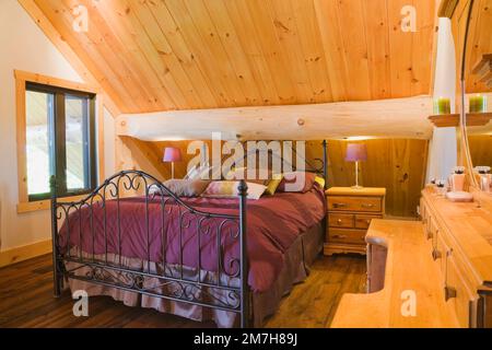 Queen-Size-Bett mit schmiedeeisernem Kopfteil und Fußbrett plus antike Holzschränke im Hauptschlafzimmer im oberen Stockwerk in einer luxuriösen Blockhütte. Stockfoto