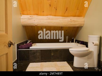 Weiße Porzellan-Toilette und Keramik-ummantelte Badewanne im Hauptbadezimmer auf der oberen Etage in einem luxuriösen skandinavischen Blockhaus. Stockfoto