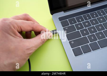 Nahaufnahme eines Mannes, der ein usb-C-Kabel an einem Laptop mit grünem Hintergrund anschließt Stockfoto
