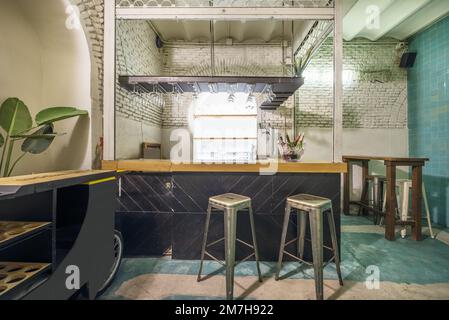 Restauranthalle mit einer Bar im industriellen Stil aus Holz und Metall, grünen Böden, Backsteinbögen und hohen Holztischen Stockfoto