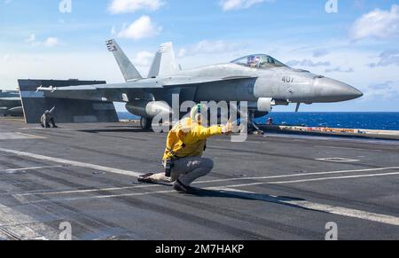 Philippinen-Meer, Internationale Gewässer. 27. Dezember 2022. Ein Navy Yellow Vest Aircraft Shooter der USA leitet ein F/A-18E Super Hornet-Kampfflugzeug, mit dem Blue Diamonds of Strike Fighter Squadron 146, das vom Flugdeck des Flugzeugträgers der Nimitz-Klasse USS Nimitz während des Routineeinsatzes am 27. Dezember 2022 in der Philippinen See gestartet werden soll. Kredit: MC2 Justin McTaggart/USA Navy/Alamy Live News Stockfoto