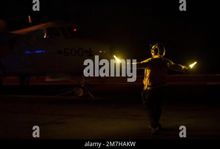 USS Nimitz, USA. 27. Dezember 2022. EIN US-AMERIKANISCHER Navy Sailor leitet ein Frühwarnflugzeug E-2C Hawkeye vom Sun Kings of Carrier Airborne Early Warning Squadron 116 während des Nachtflugbetriebs auf dem Cockpit des Flugzeugträgers der Nimitz-Klasse USS Nimitz, das am 27. Dezember 2022 Routineeinsätze in der Philippinen See durchführt. Kredit: MC2 David Rowe/U.S Navy Photo/Alamy Live News Stockfoto