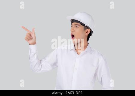 Porträt junger asiatischer Mann ist Ingenieur, der einen Helm trägt, der steht und einen isolierten weißen Hintergrund erregte, männlich ist Architekt oder Bauunternehmer, der präsentiert oder zeigt Stockfoto