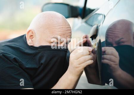 Ein Autodieb, der ein Auto klaut. Ein unverschlossener Wagen, ein Mann, der drinnen einbrechen will. Stockfoto