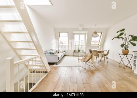 Ein Wohnzimmer mit Holzfußboden und weißen Wänden, eine offene Treppe, die in die zweite Etage führt, ist sichtbar Stockfoto