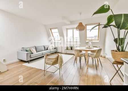 Ein Wohnzimmer mit weißen Wänden und Holzfußboden, einschließlich eines grauen Sofas in der Mitte des Zimmers Stockfoto
