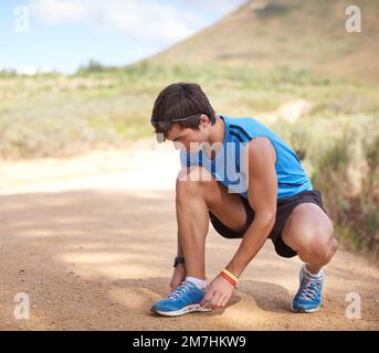 Es geht nichts über frische Luft und Bewegung. Ein junger Mann, der seine Schuhschnürsenkel vor seinem Lauf auf einer Schotterstraße fesselt. Stockfoto