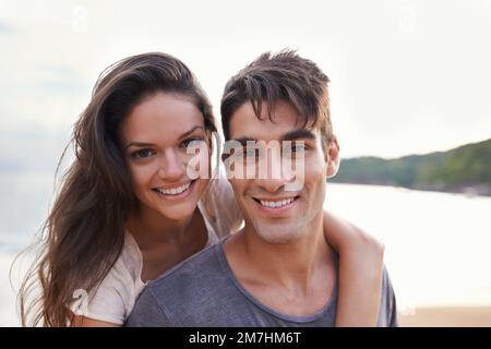 Sie sind unzertrennlich. Eine kurze Aufnahme eines jungen Mannes, der seiner Freundin eine Huckepackfahrt am Strand gibt. Stockfoto