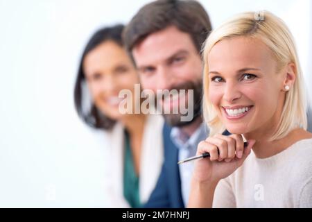 Sie denken an Geschäftserfolg. Porträt einer attraktiven Geschäftsfrau, die vor der Kamera lächelt, mit einer Reihe von Geschäftsleuten hinter ihr. Stockfoto