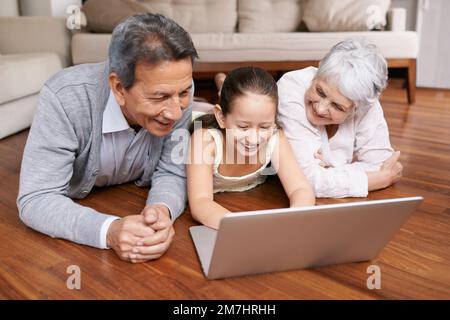 Erstellen eines Social-Media-Profils für Oma und Opa. Ein junges Mädchen und ihre Großeltern liegen auf dem Boden und schauen auf einen Laptop. Stockfoto