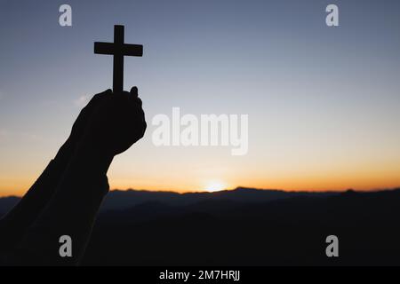 Silhouette von den Händen halten Holzkreuz auf Sonnenaufgang Hintergrund, Kruzifix, Symbol des Glaubens. Stockfoto