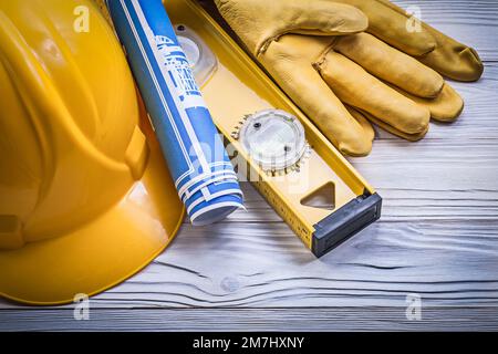 Zusammensetzung von Sicherheitshandschuhen Bauhelm blau gerollte Blaupausen Baustufe auf Holzbrett. Stockfoto