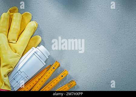 Zusammensetzung von Arbeitshandschuhen Blaupausen Holzmeter auf Betonhintergrund Baukonzept. Stockfoto