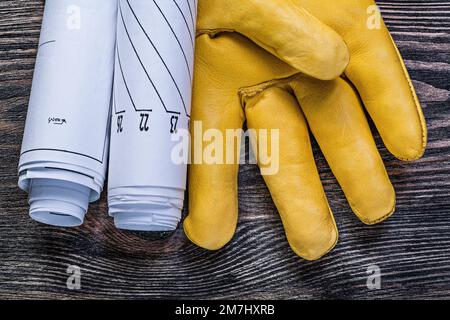 Zusammenstellung von Ledersicherheitshandschuhen gerollte Konstruktionszeichnungen auf Holzbrettbaukonzepten. Stockfoto