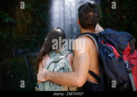 Einfach spektakulär. Rückblick auf ein junges Paar, das zusammensteht und einen Wasserfall ansieht. Stockfoto