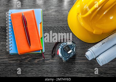 Baupläne Maßband Bauhelm Notizblöcke Stift auf Holzbrett. Stockfoto