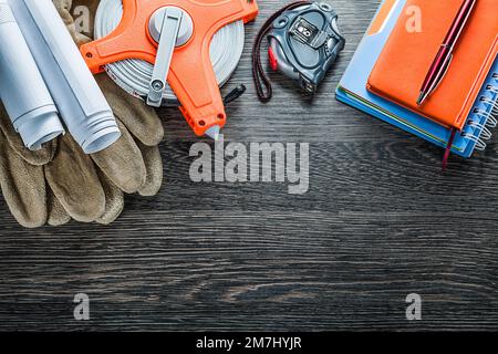 Technische Zeichnungen Maßband Sicherheitshandschuhe Notizblock Stift auf Holzbrett. Stockfoto