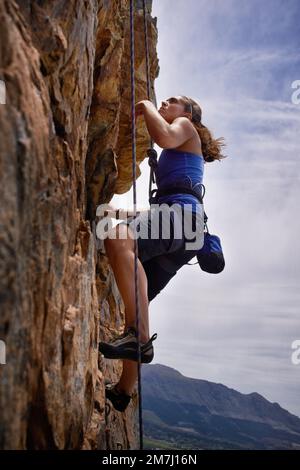 Auf dem Weg den Berg hinauf. Seitenansicht einer jungen Frau beim Klettern. Stockfoto