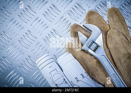 Sicherheitshandschuhe gerollte Konstruktionszeichnungen Rollgabelschlüssel auf gerilltem Metallhintergrund. Stockfoto