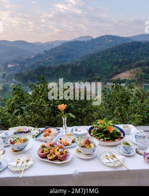 Frühstückstisch in den Bergen von Thailand Chiang Mai, ein hölzerner festlicher Tisch mit hausgemachten Speisen und Getränken, frischem Obst und Blumen unter einer Kiefer an einem sonnigen Tag. Luxuriöses Frühstück. Stockfoto