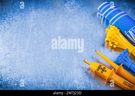 Gelber elektrischer Tester Kabelbinder blaue Baupläne auf metallischem Hintergrund Stromkonzept. Stockfoto